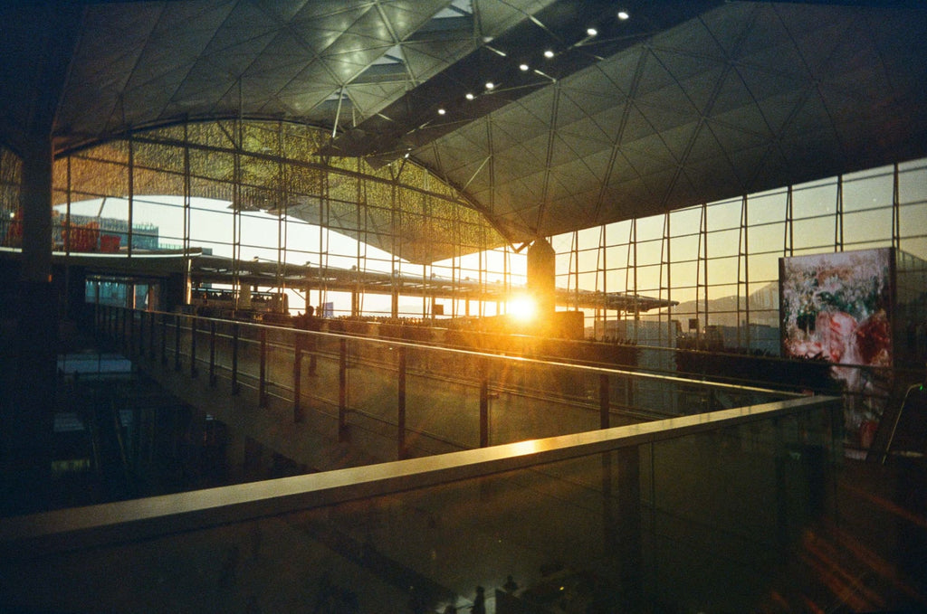 The sun sets through the glass windows of a modern, geometrically structured airport terminal.