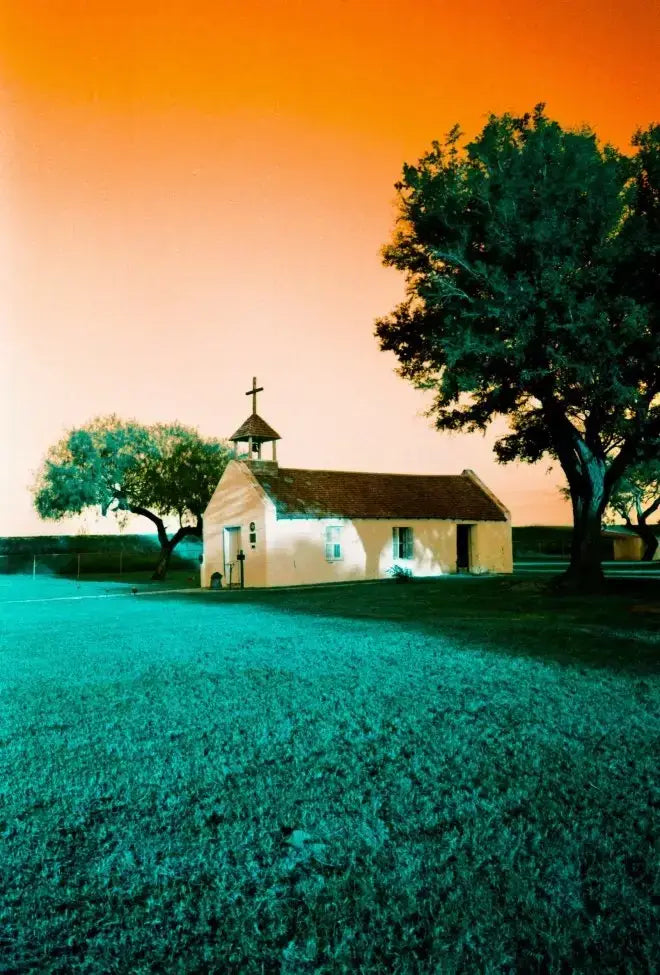 Small cream church with brown roof under orange sky on Lomography Turquoise film