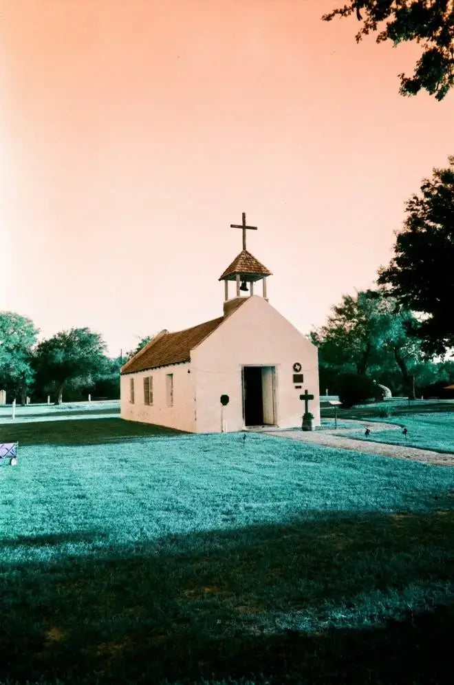 Small white church on Lomography turquoise film under pink sky