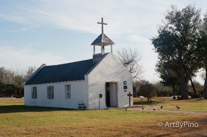 White stucco Texas church with gray shingled roof and cross tower, view fullsize