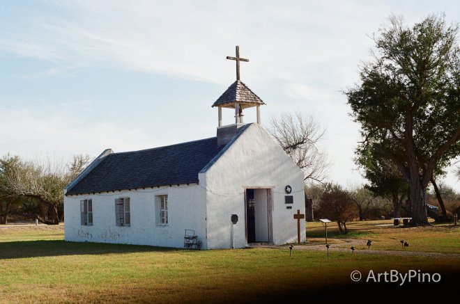 White stucco Texas church with gray shingled roof and bell tower, view fullsize