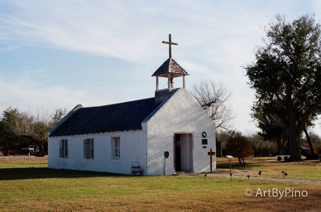 White stucco Texas church with dark shingled roof and bell tower, view fullsize