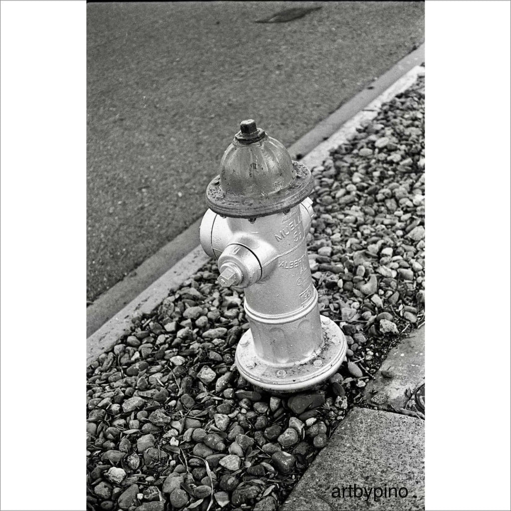 A classic silver fire hydrant with a domed top and bolted caps, standing on a bed of gravel.