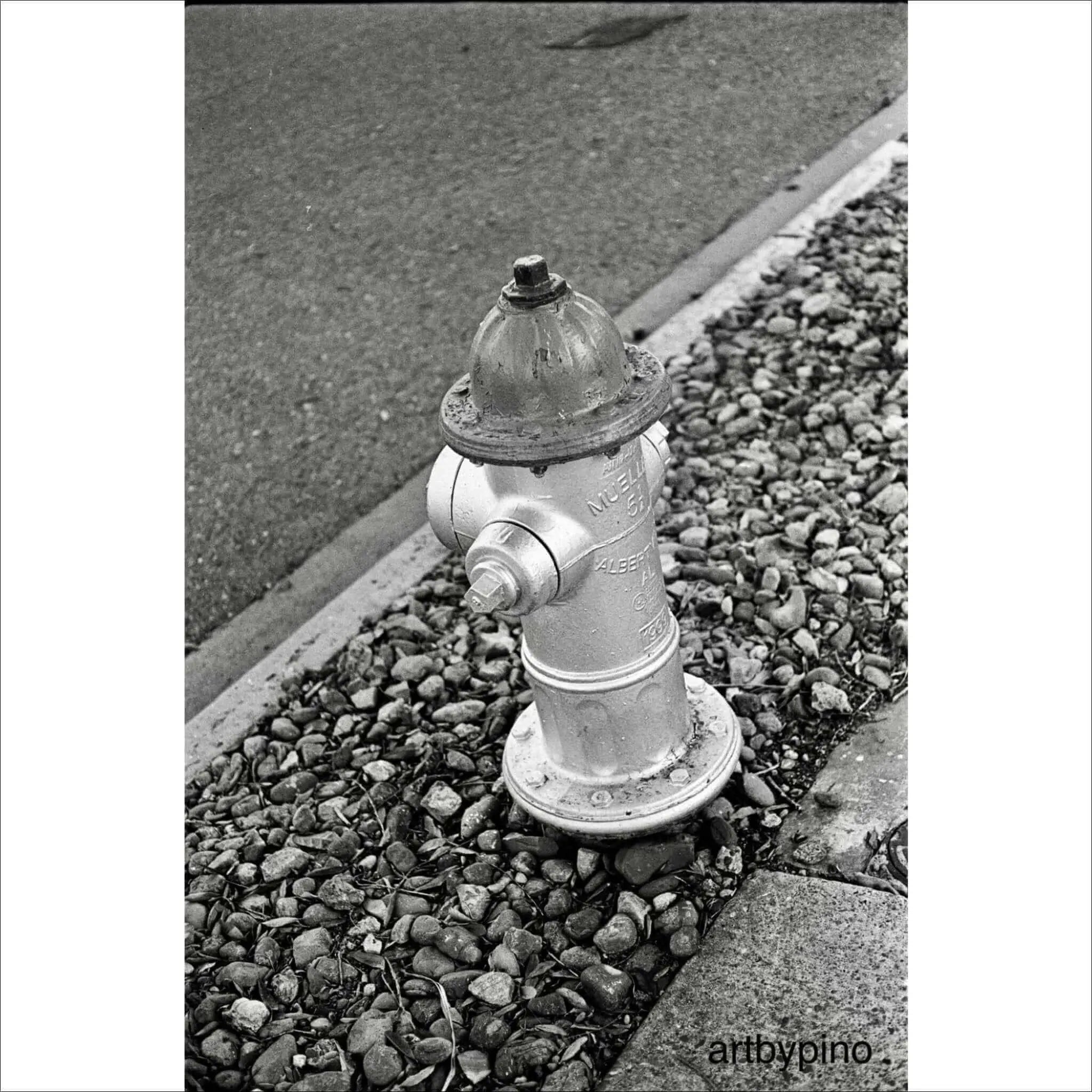 A classic silver fire hydrant with a domed top and bolted caps, standing on a bed of gravel.
