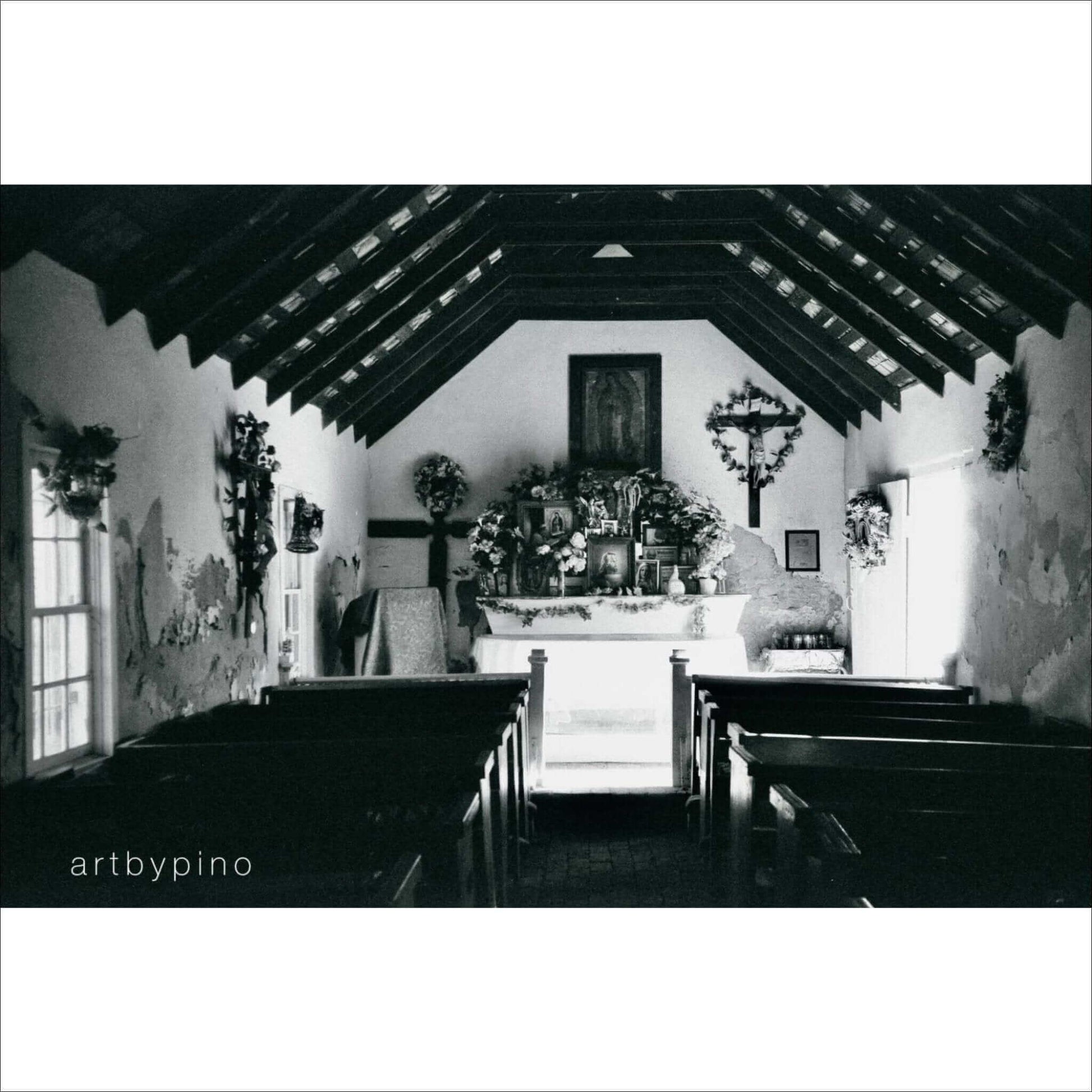 Interior of a quaint church with wooden benches and an altar, captured in black and white photography.