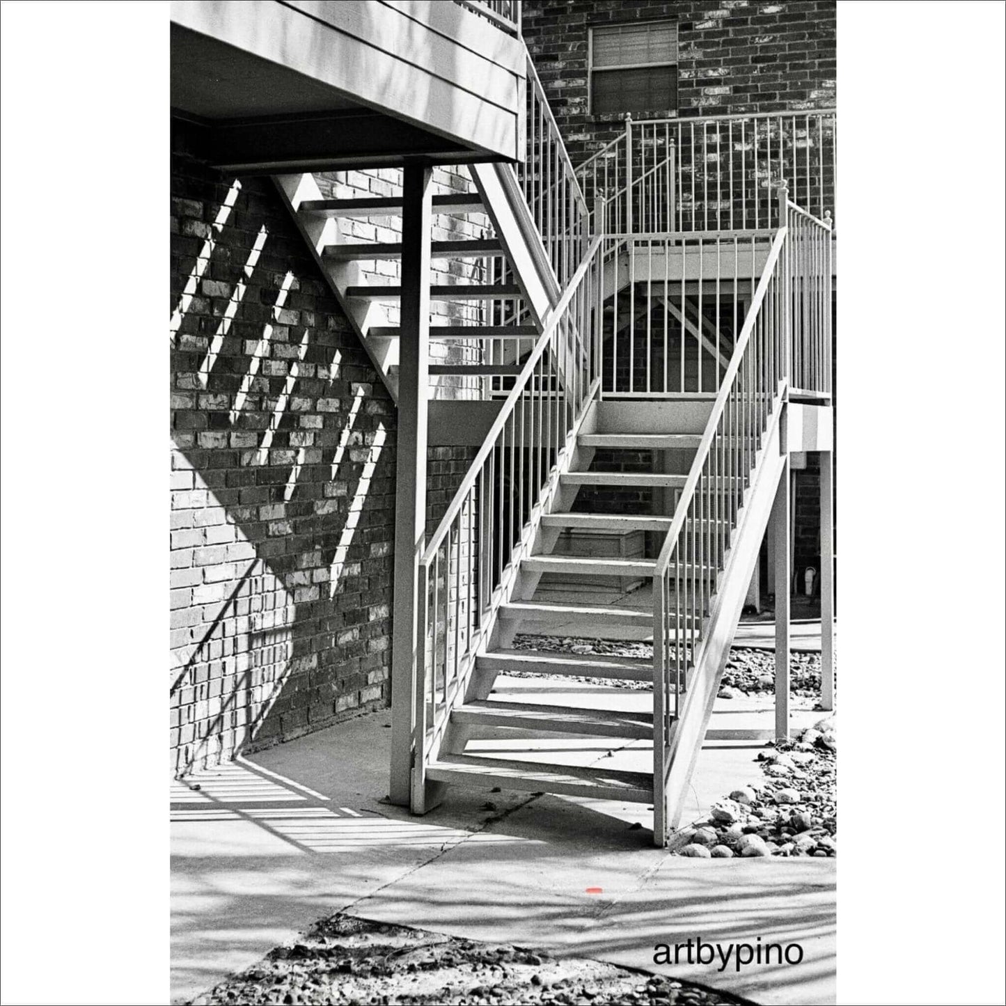 Black and white photo of exterior stairs with shadows cast on brick wall.