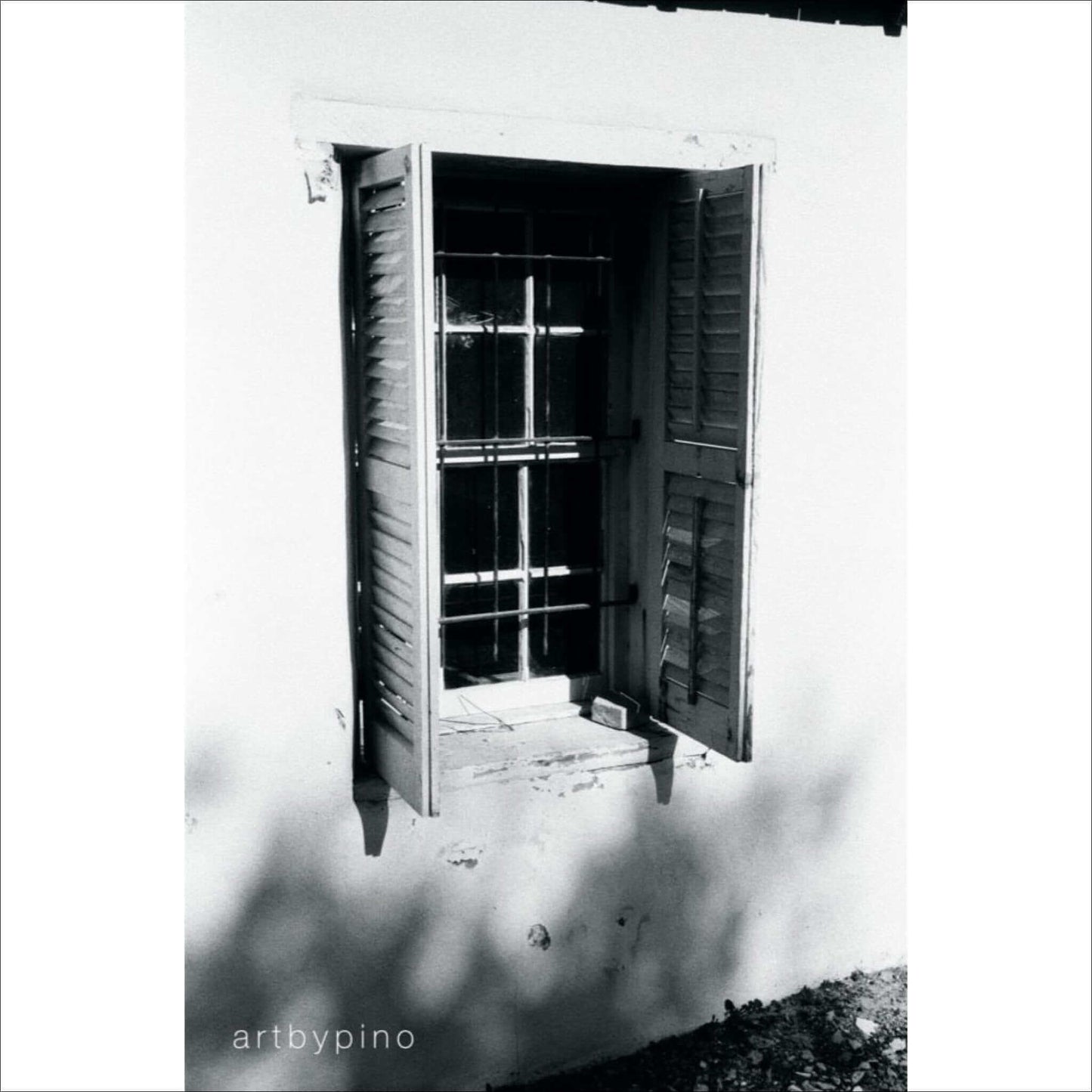 Black and white photograph of a shuttered window with sunlight casting shadows on the wall.