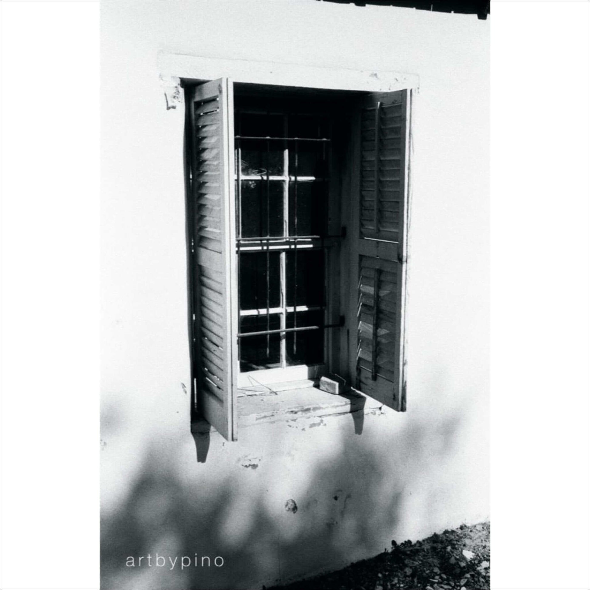 Black and white photograph of a shuttered window with sunlight casting shadows on the wall.