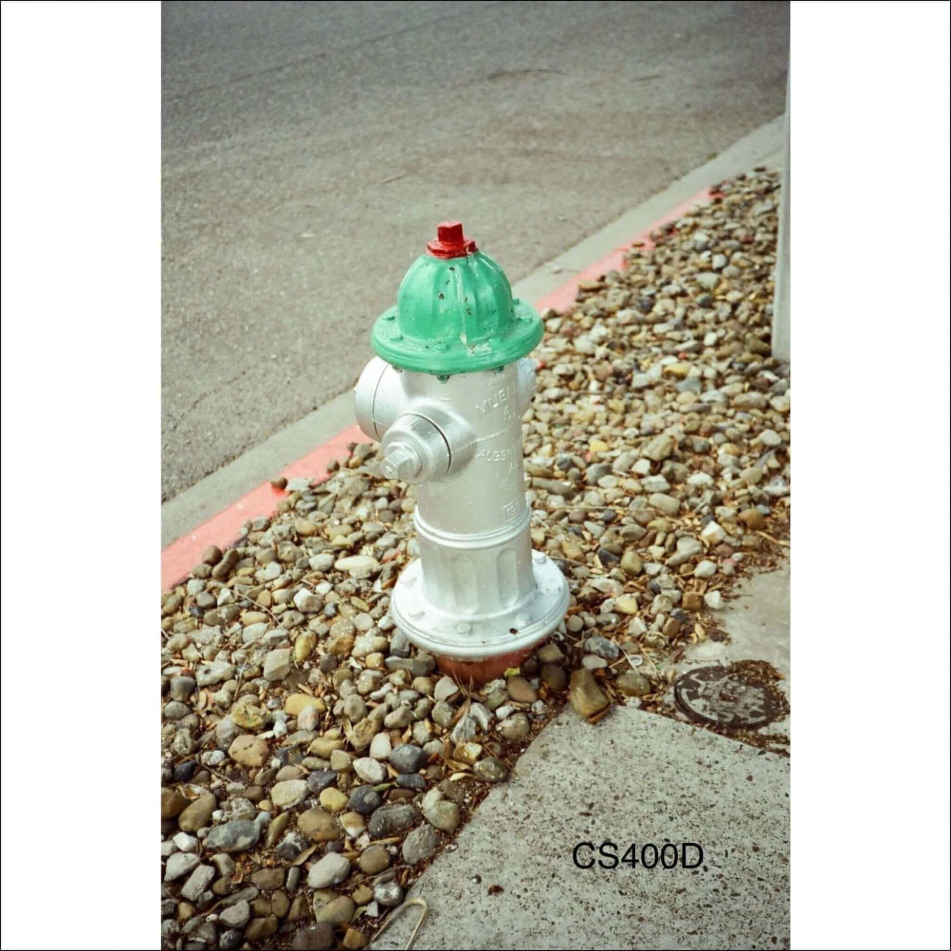 Colorful fire hydrant with a green cap on a gravel surface.
