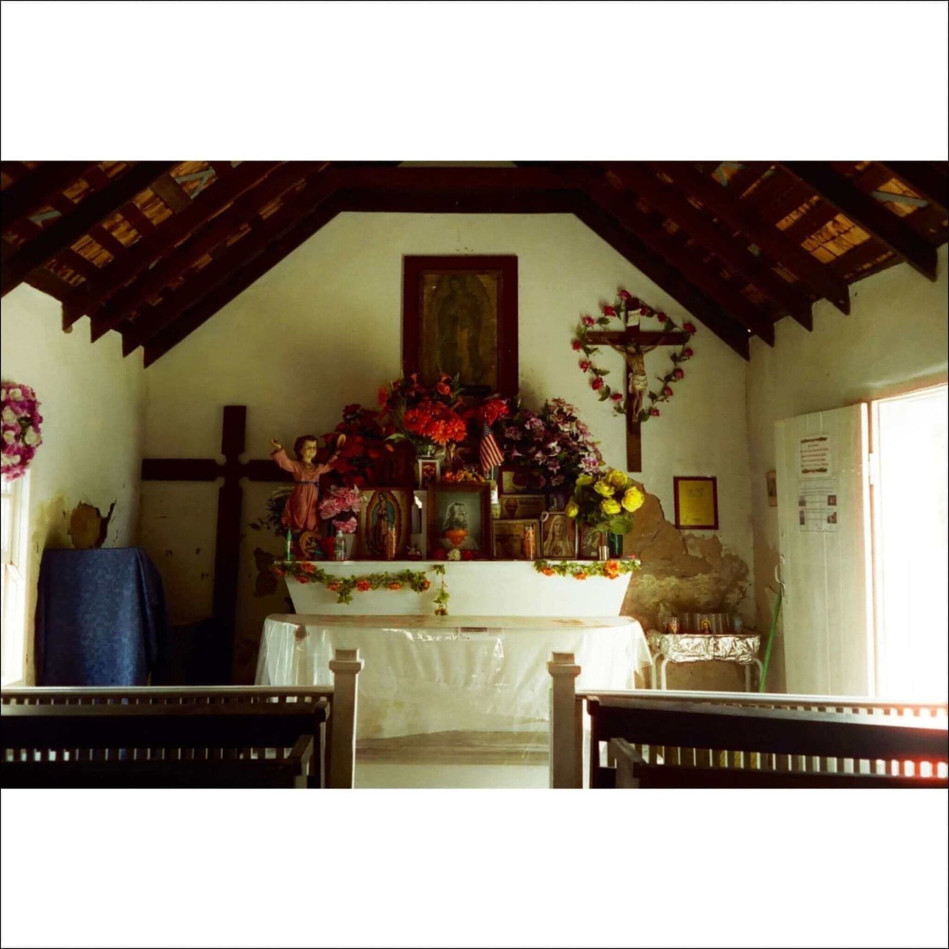 Interior of a quaint church featuring an altar adorned with flowers, religious statues, and wooden beams.