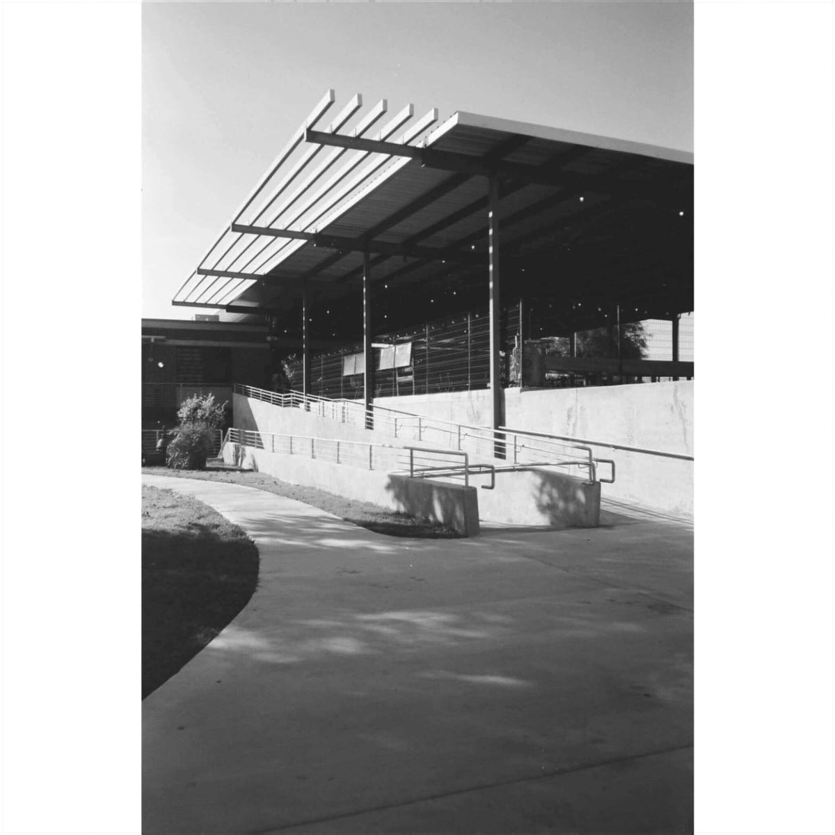 Black and white photograph of a modern building with a ramp and covered outdoor area.