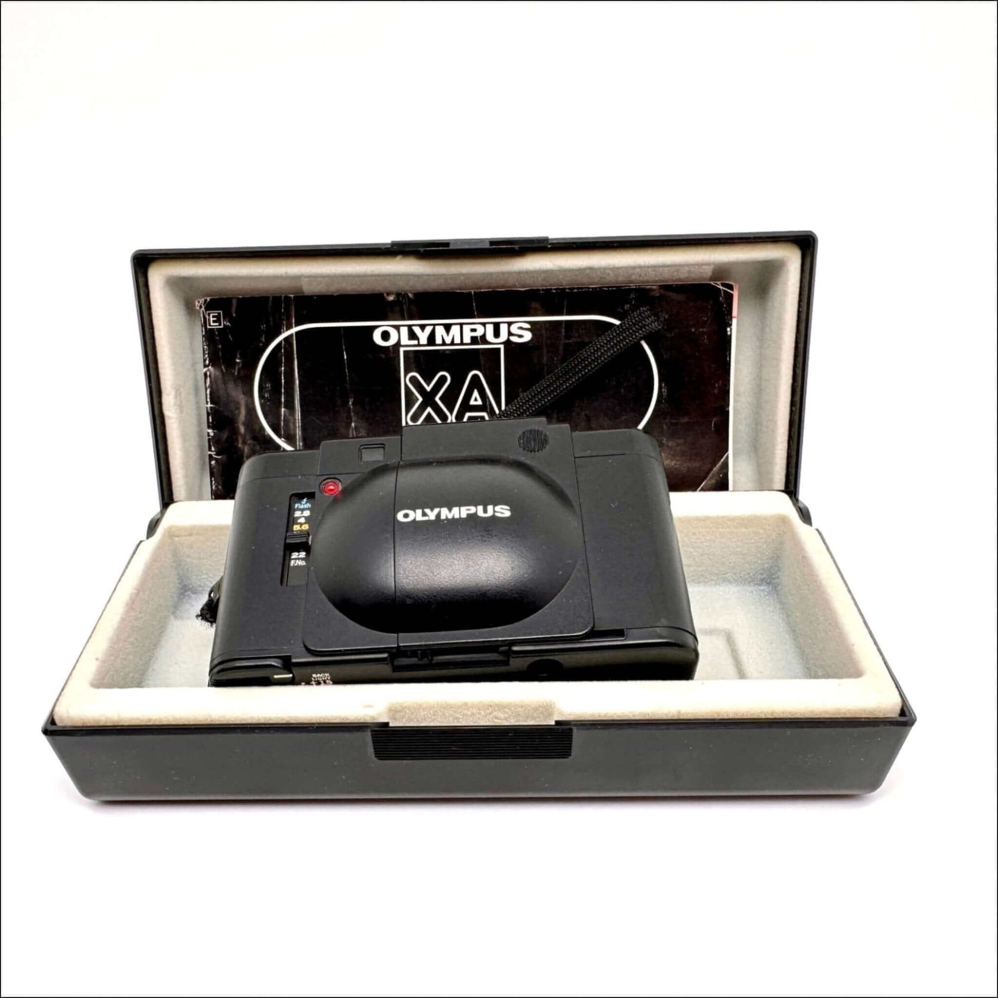 Olympus XA vintage 35mm film camera in original case with instruction manual, showcasing cosmetic quality and features.