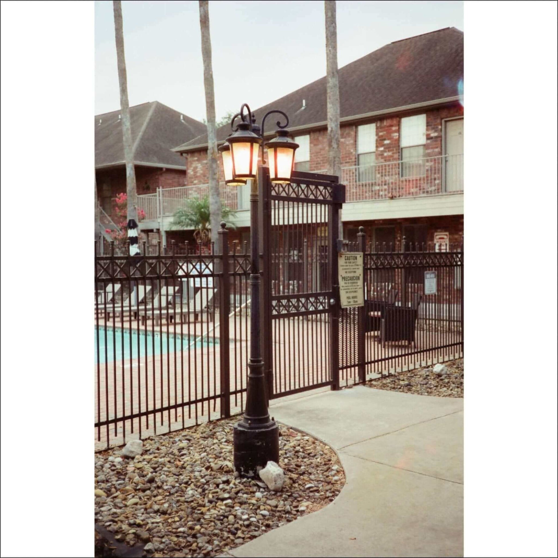 Classic black lamp post illuminating a pool area, surrounded by a fenced pathway and residential buildings.