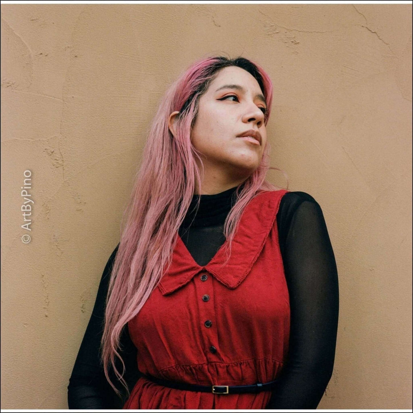 Portrait of a woman with pink hair wearing a red dress against a neutral background, conveying a stylish and artistic vibe.